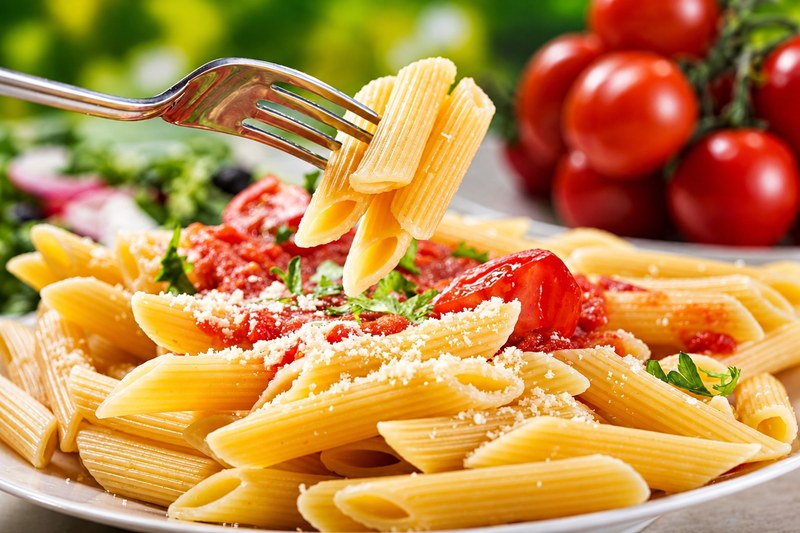 A fork lifting penne from a plate of penne in tomato sauce with grated parmesan